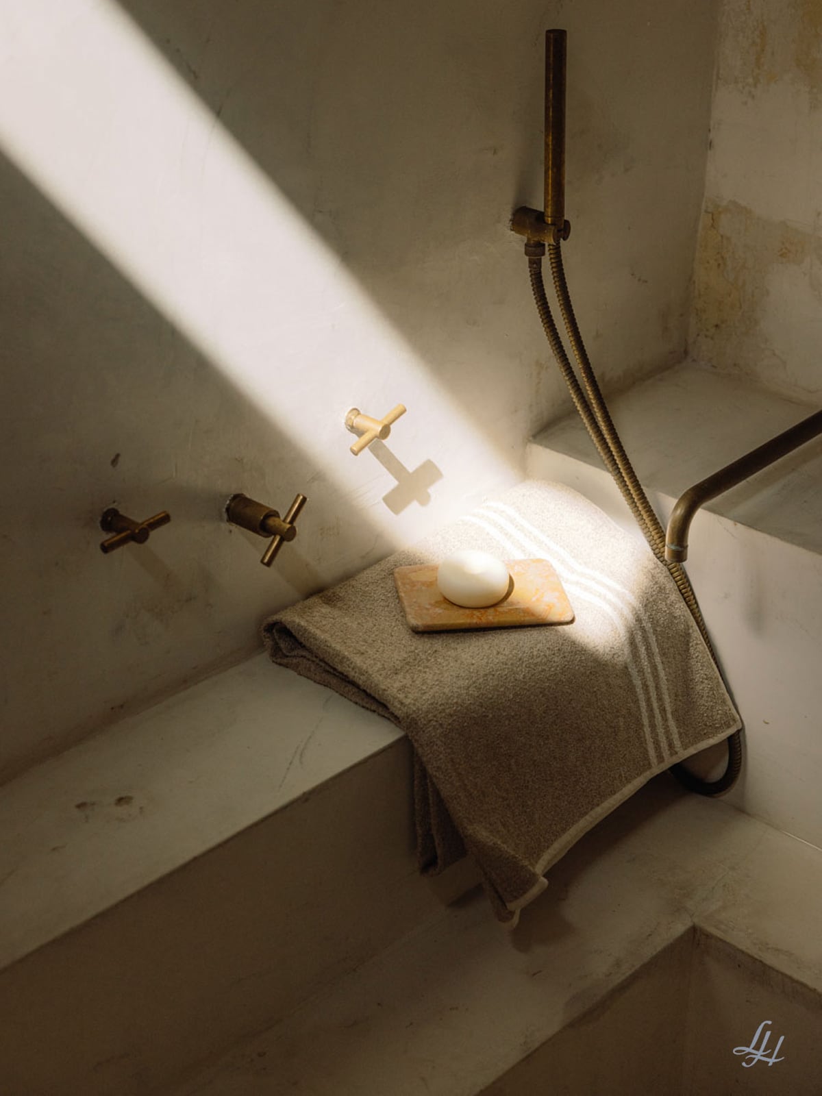 Ein Leinenfrotté-Handtuch und ein Stück Seife liegen auf dem Wannenrand, während das Sonnenlicht über elegante Messingarmaturen hereinstrahlt.