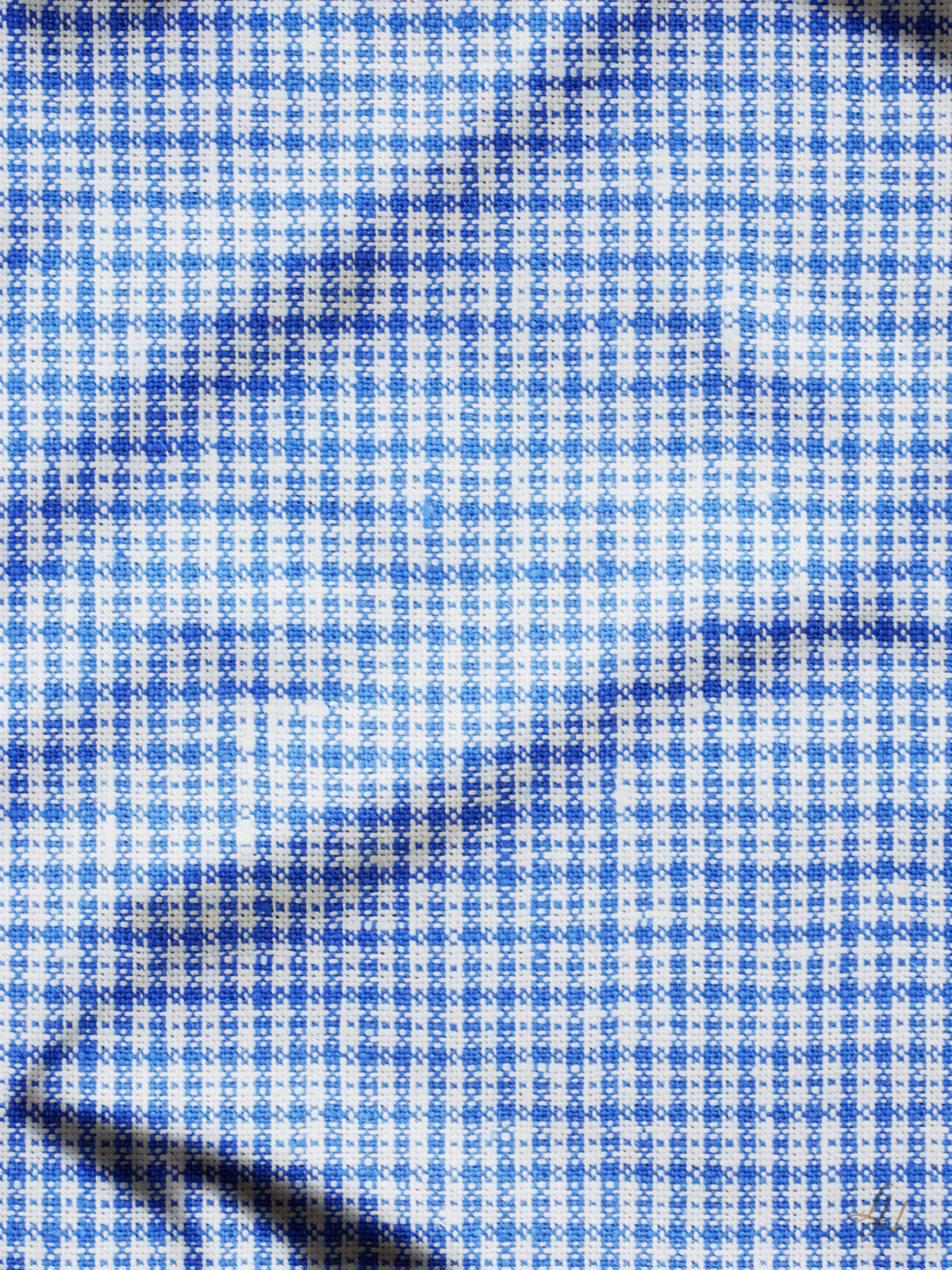 Nahaufnahme eines Stoffes mit blau-weißem Karomuster. Der Stoff hat sichtbare Knicke und Falten, die subtile Schatten und Texturen auf der Oberfläche erzeugen.