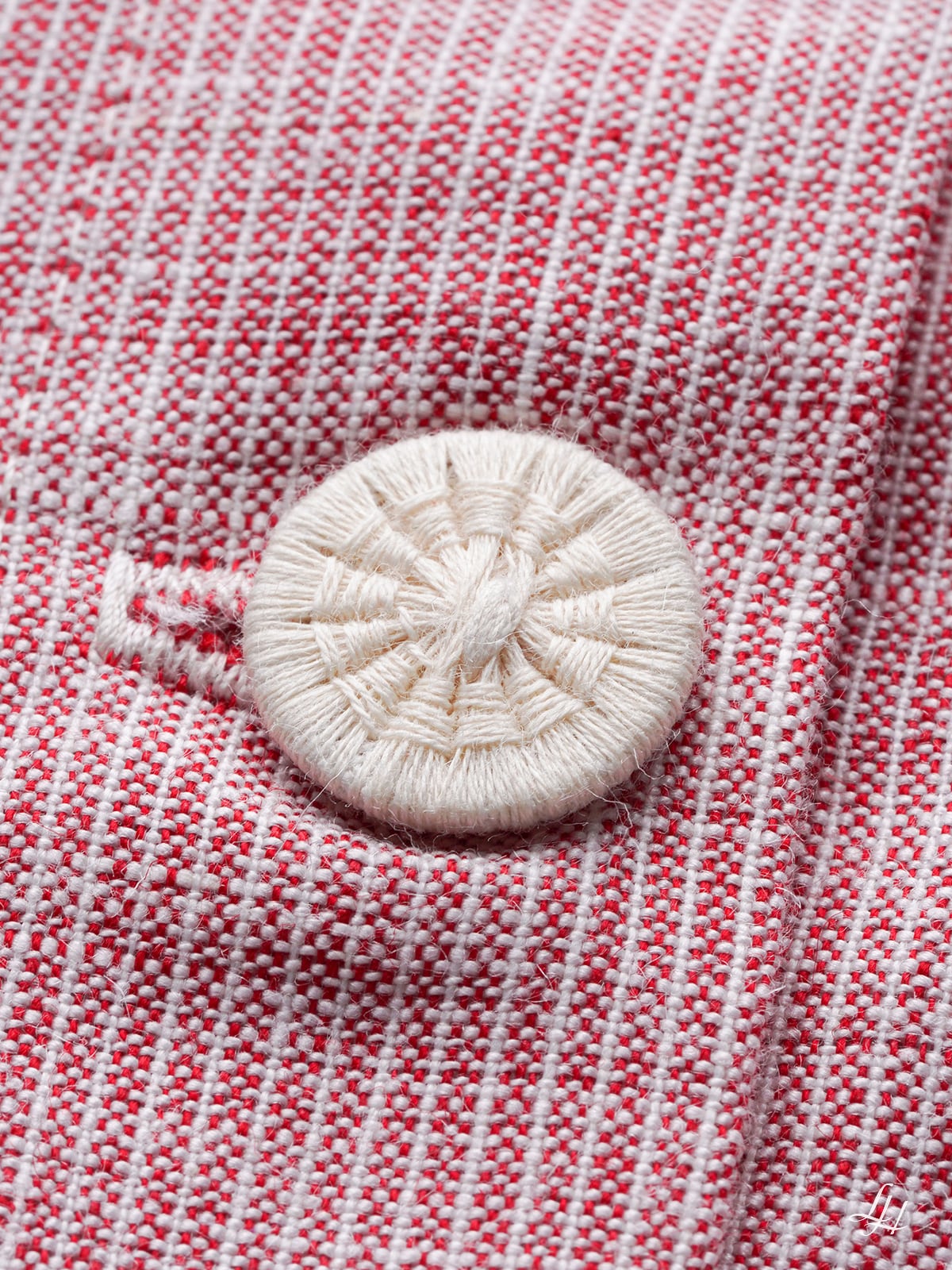 Nahaufnahme eines runden, weißen, gewebten Knopfes, der auf Nadelstreifen-Stoff aufgenäht ist, mit einem passenden genähten Knopfloch.