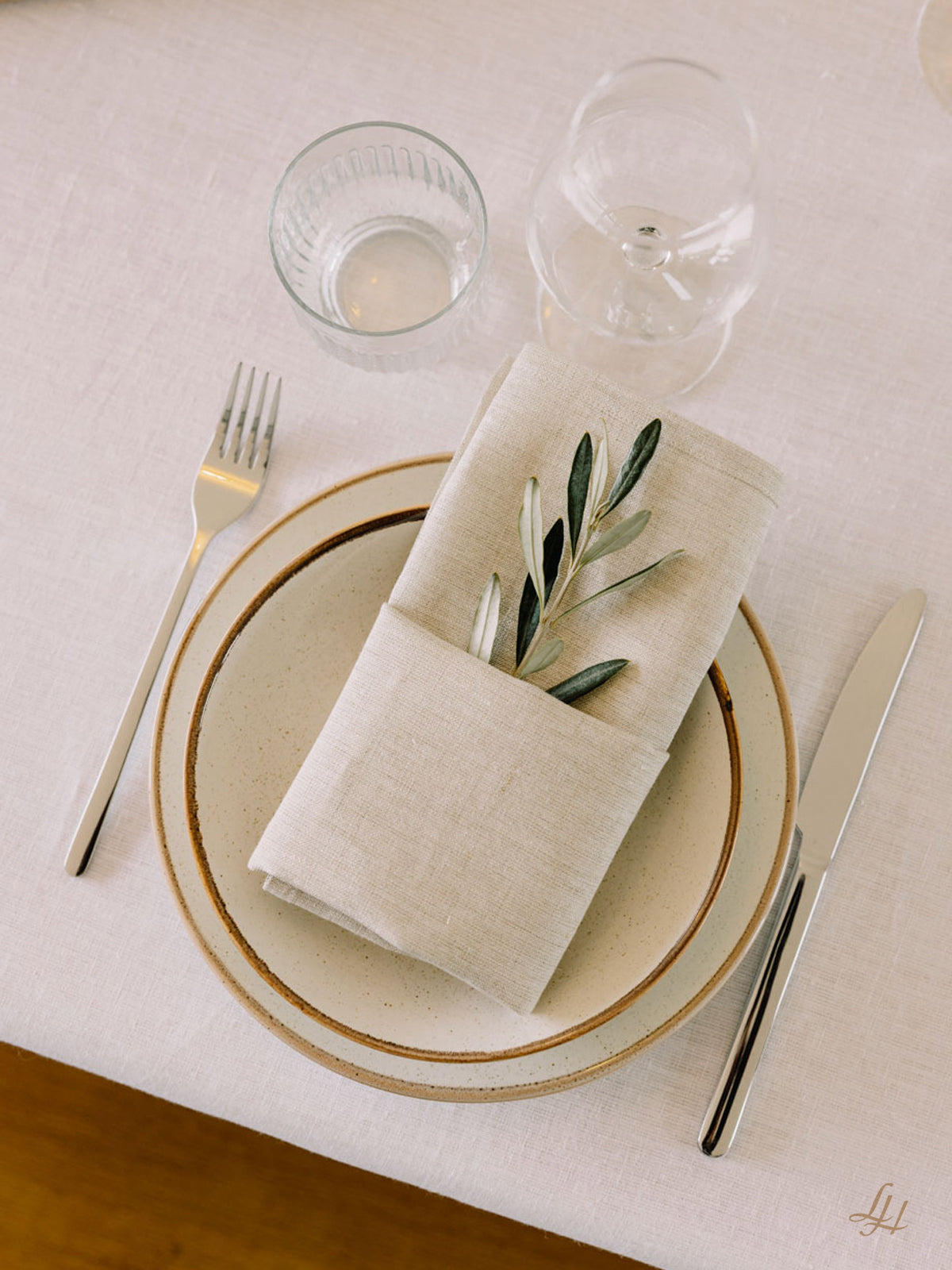 Ein Tischset mit einer Gabel, einem Messer, zwei Tellern, einem Glas und nachhaltigen Leinen-Servietten mit grünen Blättern darin.