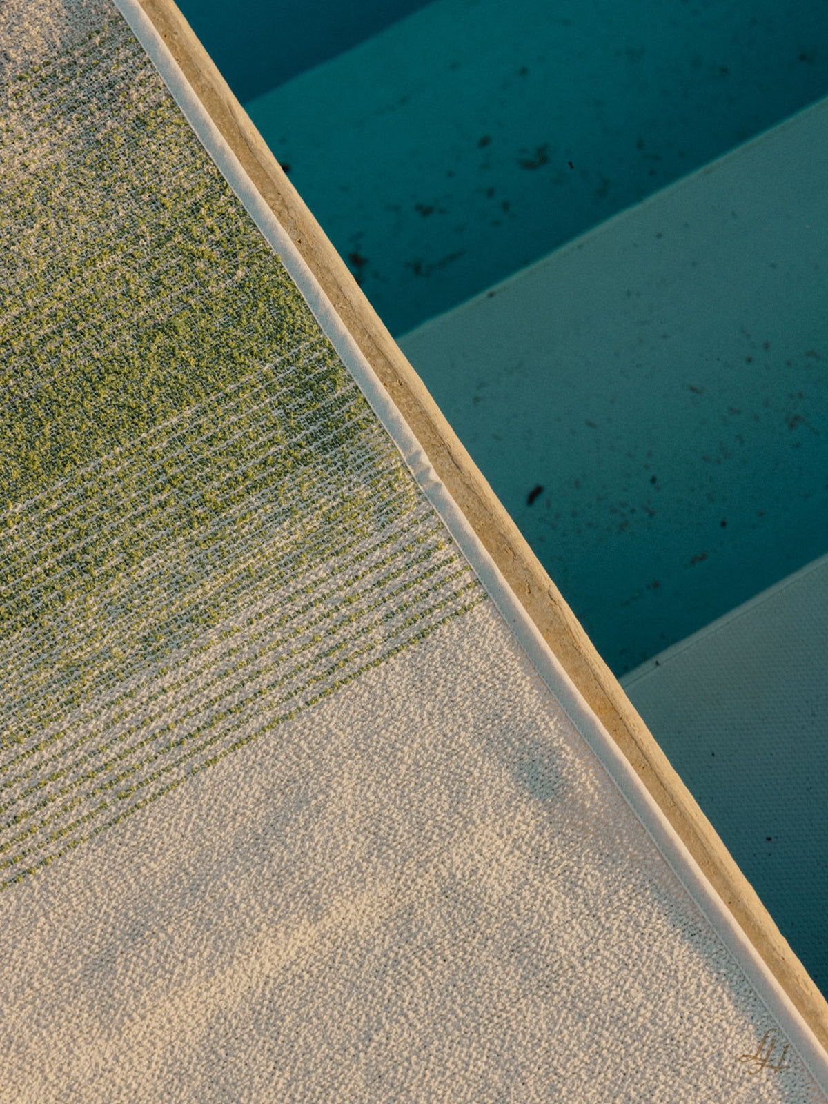 Nahaufnahme eines strukturierten Leinenhandtuchs in der Nähe von blauen Poolstufen, wobei im Wasser etwas Schmutz und Ablagerungen sichtbar sind.