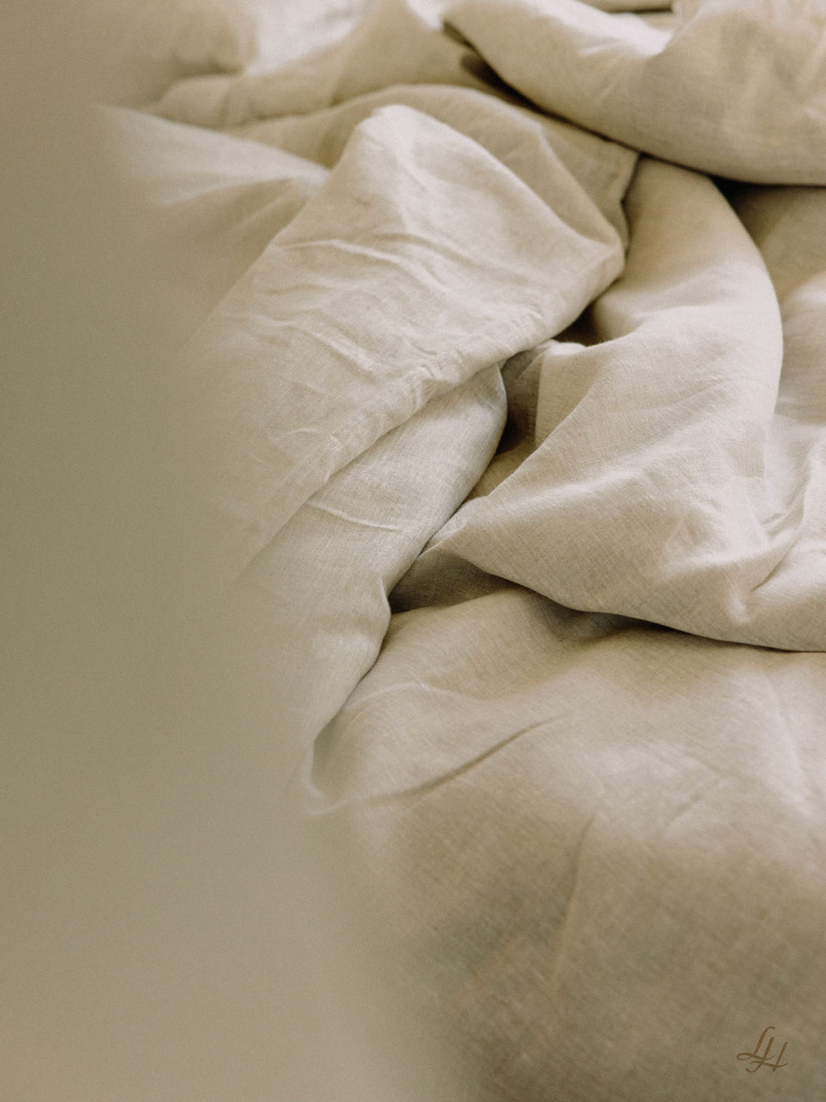 Eine Nahaufnahme von zerknitterter Reinleinen-Bettwäsche, mit weichem, natürlichem Licht und sichtbarer, hypoallergener Stoffstruktur.