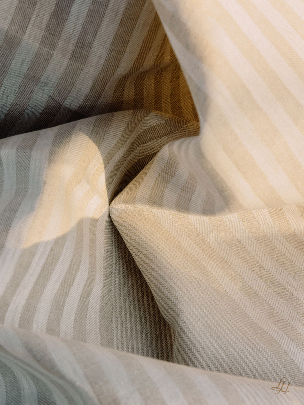 Nahaufnahme eines creme- und beigefarbenen gestreiften europäischen Leinenstoffs mit sichtbaren Falten und weichen Schatten.