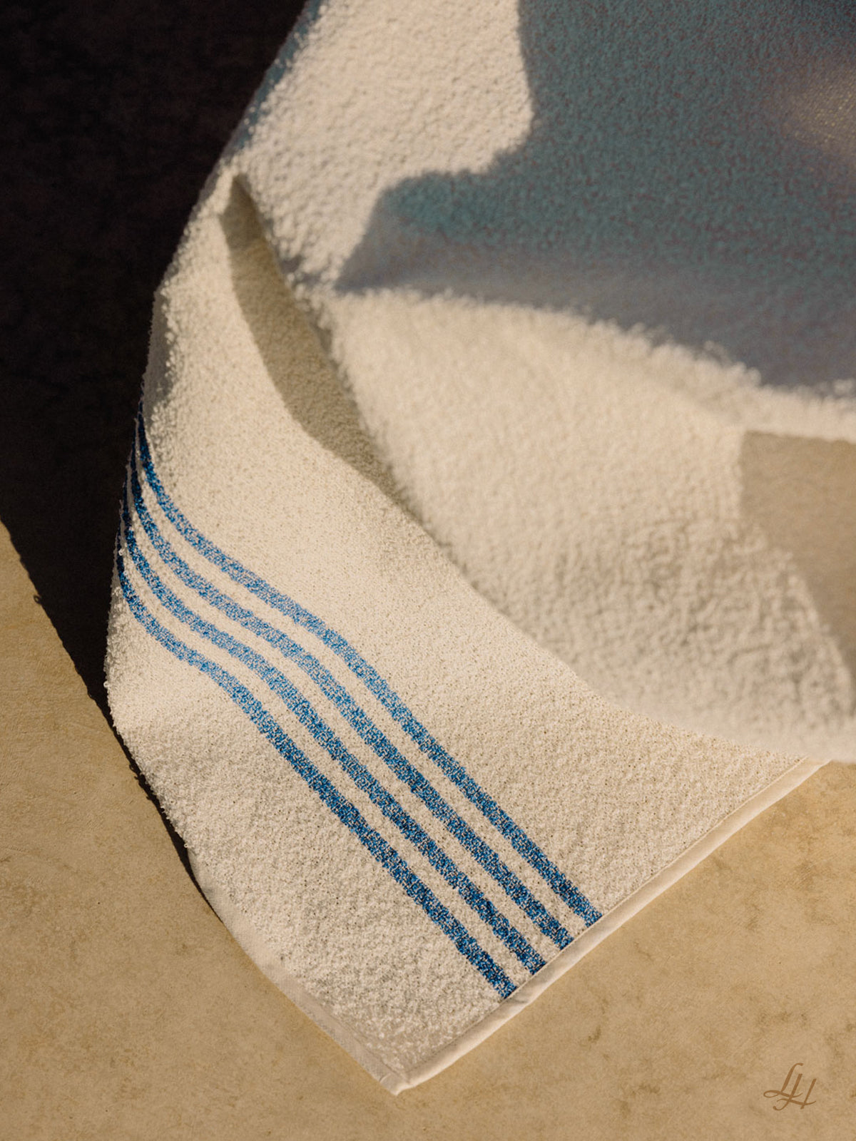 Ein Leinenfrotté-Handtuch mit blauen Streifen ist auf einer Fläche drapiert, Sonnenlicht und Schatten heben das europäische Leinen hervor.