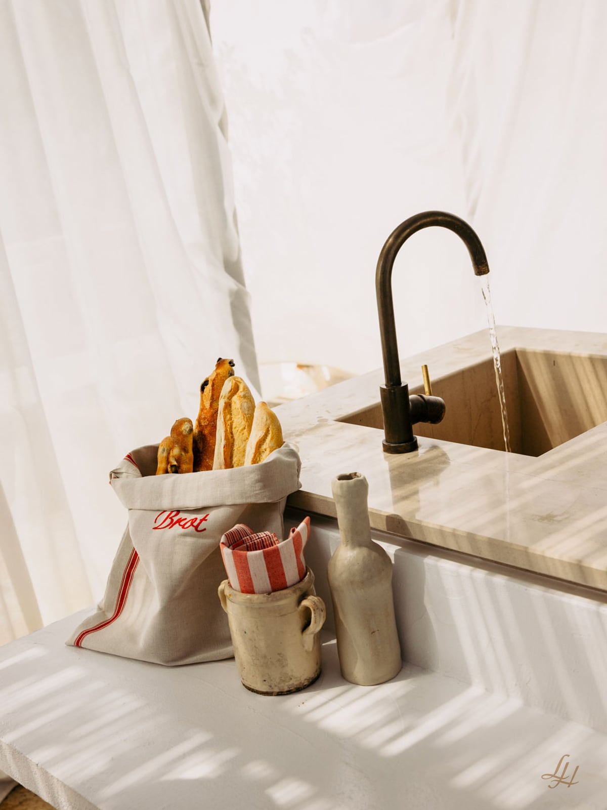 Ein Waschbecken aus Marmor, ein schwarzer Wasserhahn und eine Brotbeutel-Halbleine für natürliche Brotaufbewahrung auf einer weißen Arbeitsplatte mit Baguettes.