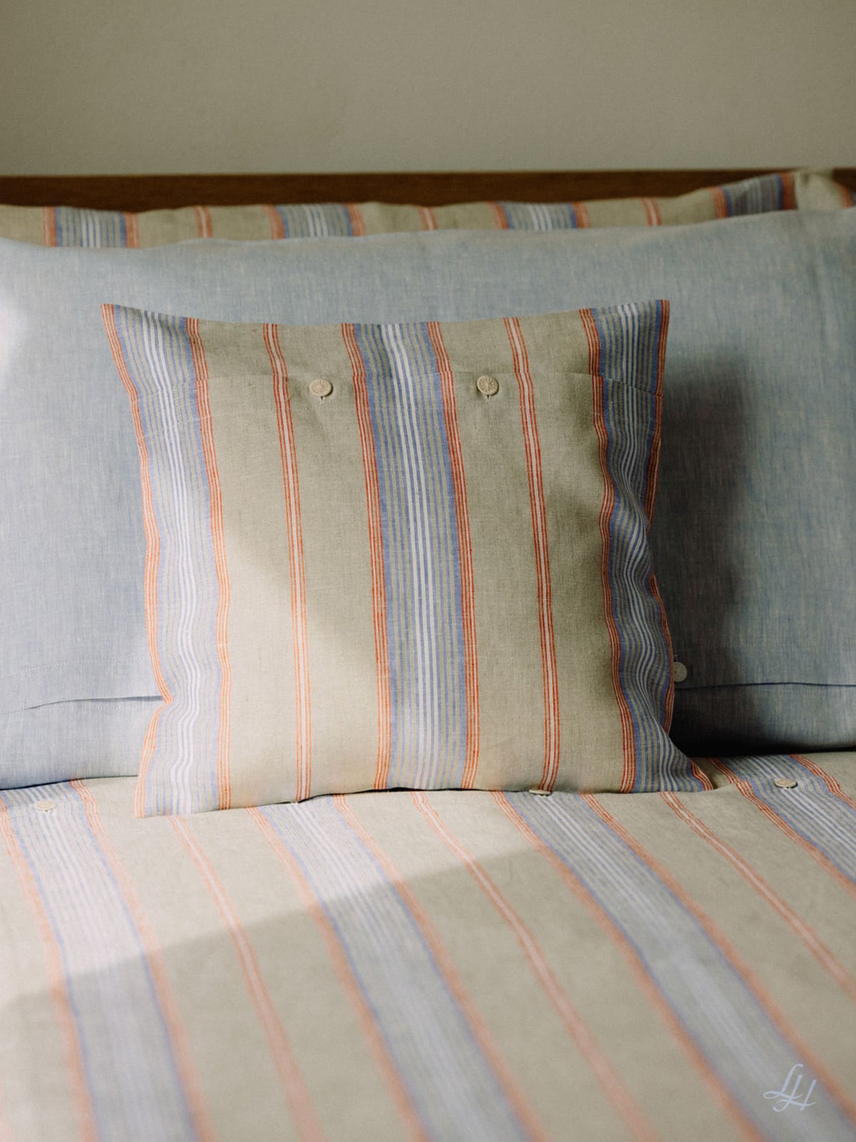 Ein quadratisches hypoallergenes Kissen mit blauen und orangefarbenen Streifen und zwei Knöpfen liegt auf einem ordentlich gemachten Bett mit passender Bettwäsche.