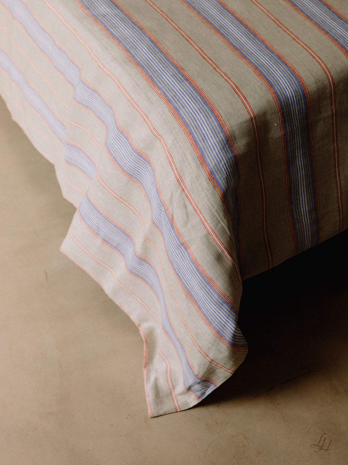 Ein Bett mit hypoallergener Leinenbettwäsche in beige, blau und rot gestreift, auf einem glatten, hellen Boden.