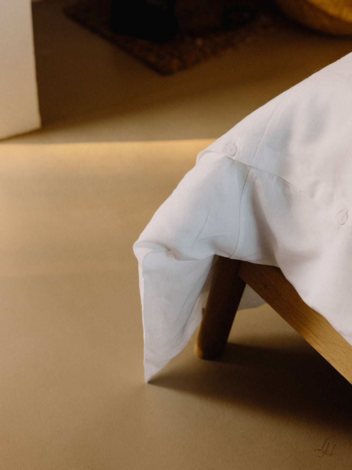 Eine Nahaufnahme einer Bettecke mit hypoallergener Leinenbettwäsche, einem hölzernen Bettrahmen und einem beigen Fußboden.