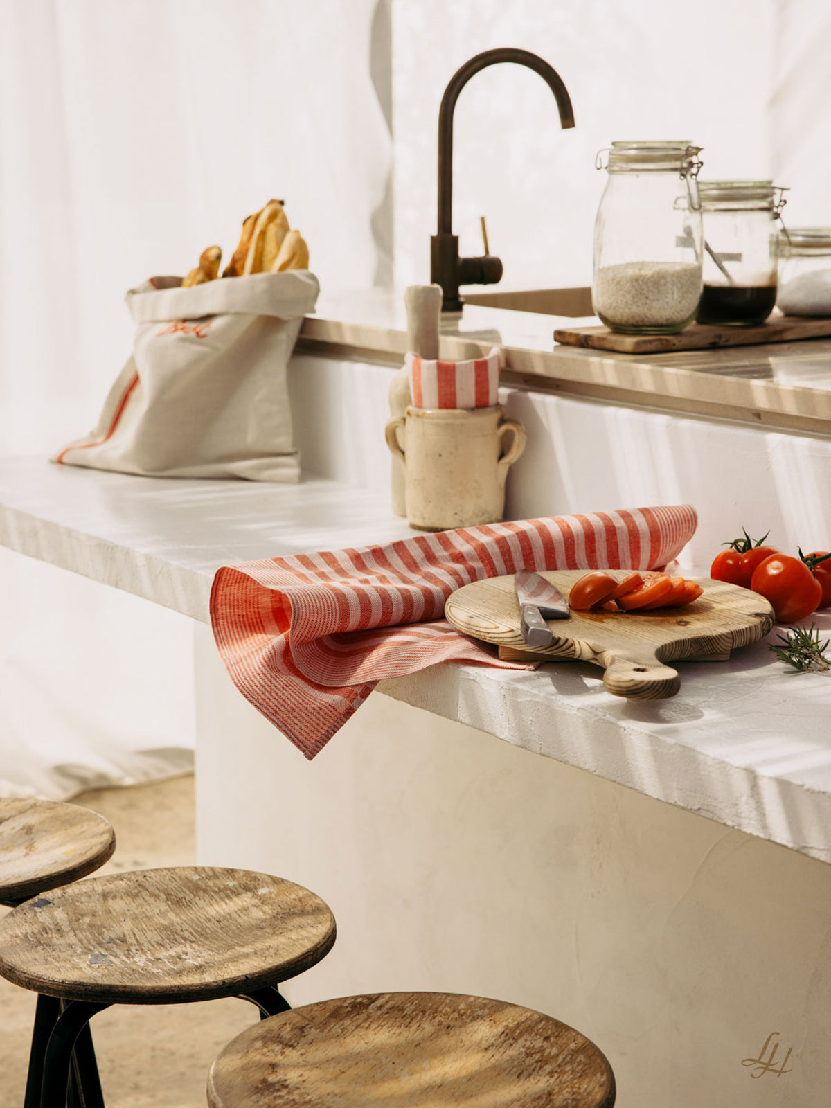 Eine Küchentheke mit Brot, Gläsern und Tomaten, akzentuiert durch Reinleinen-Geschirrtücher in klassischem Streifendesign.