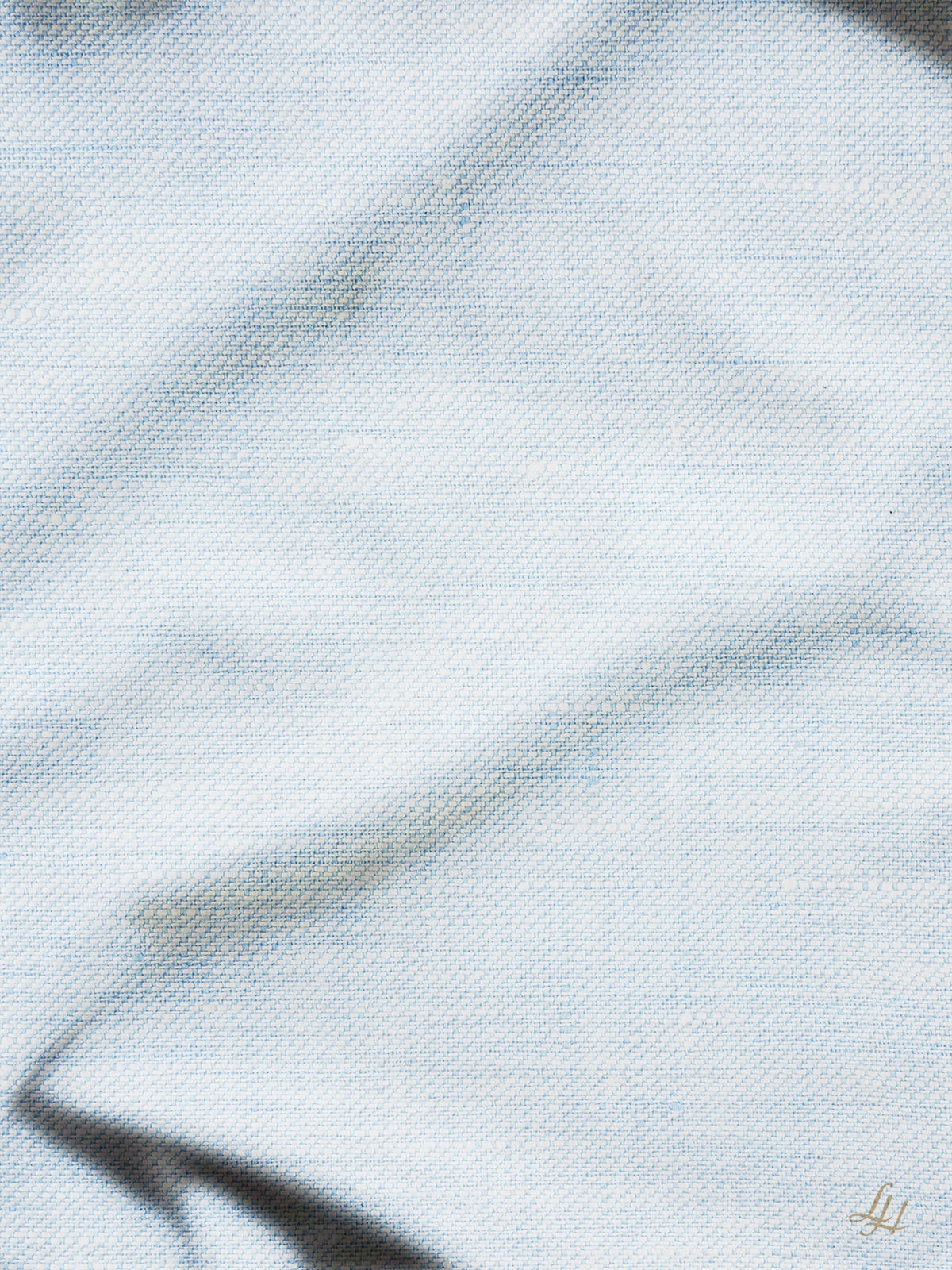 Hellblauer Jeansstoff mit sichtbarer Textur in Köperbindung, mit sanften Falten und subtilen Highlights auf der Oberfläche.