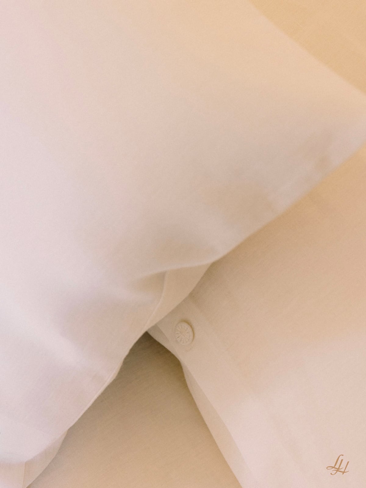 Zwei atmungsaktive weiße Kissenbezüge Leinen liegen auf einem Bett, eines mit einem Knopf und einem kleinen Monogramm in der Ecke.