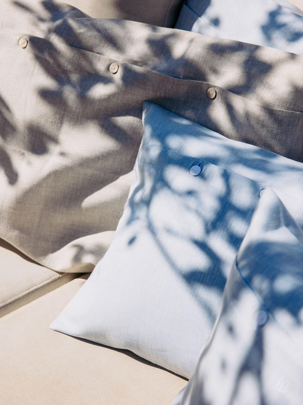 Nahaufnahme von beigefarbenen und hellblauen Kissen auf einem Sofa, mit natürlichem Sonnenlicht und Schatten - hergestellt aus europäischem Flachs.