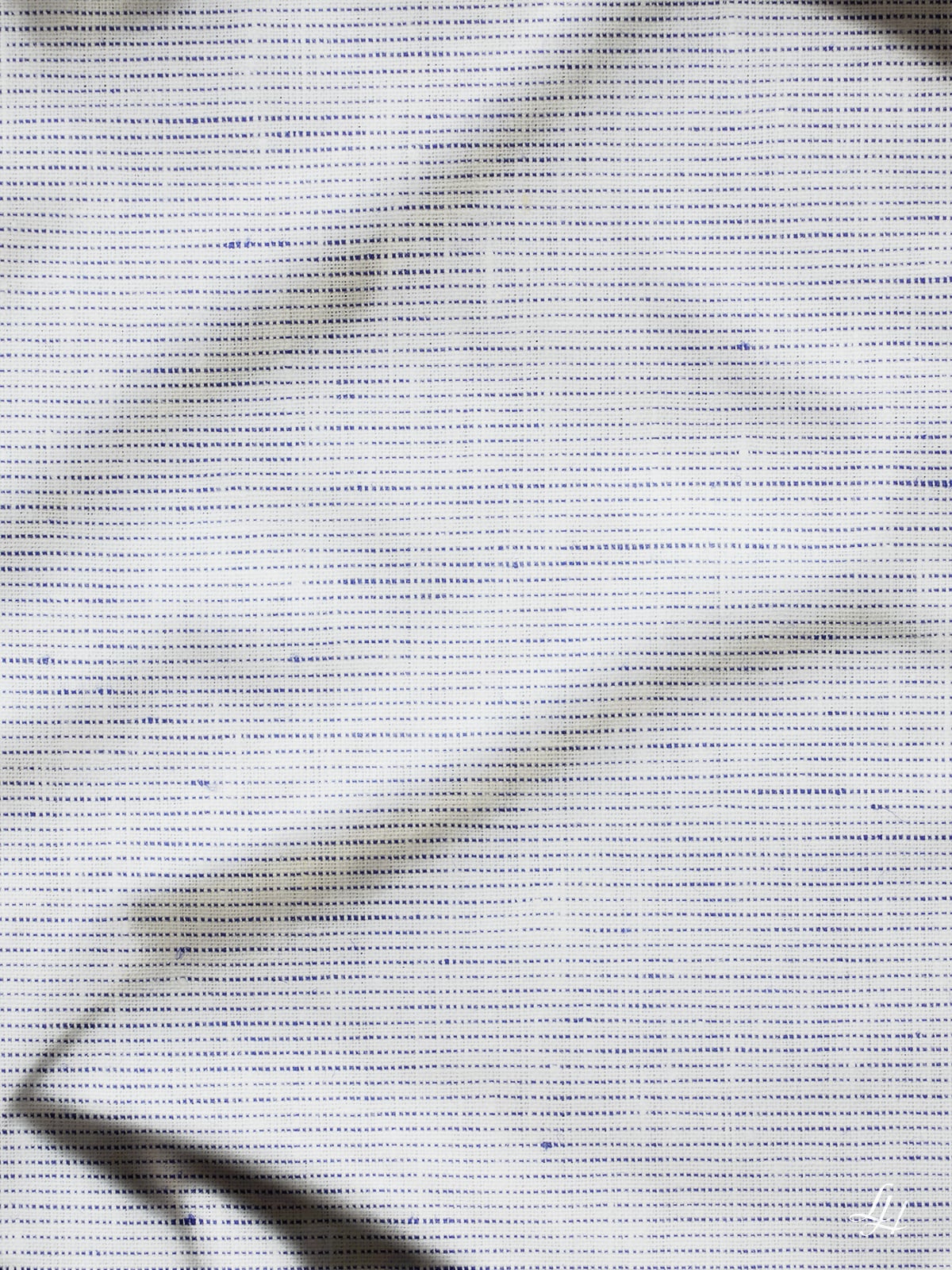 Eine Nahaufnahme von Leinenbettwäsche aus europäischem Flachs mit sichtbarer Textur, kleinen Punkten und diagonalen Falten, die weiche Schatten werfen.