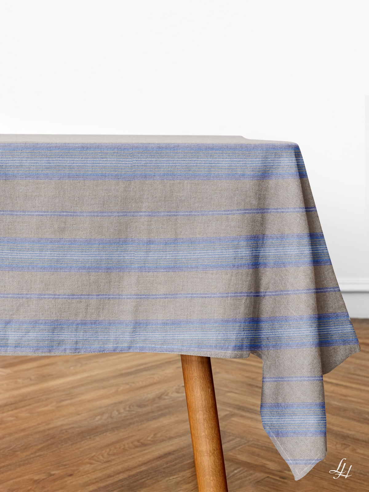 Ein rechteckiger Tisch mit hypoallergener Leinen-Tischwäsche in beige-blauen Streifen steht auf einem Holzboden vor einer weißen Wand.