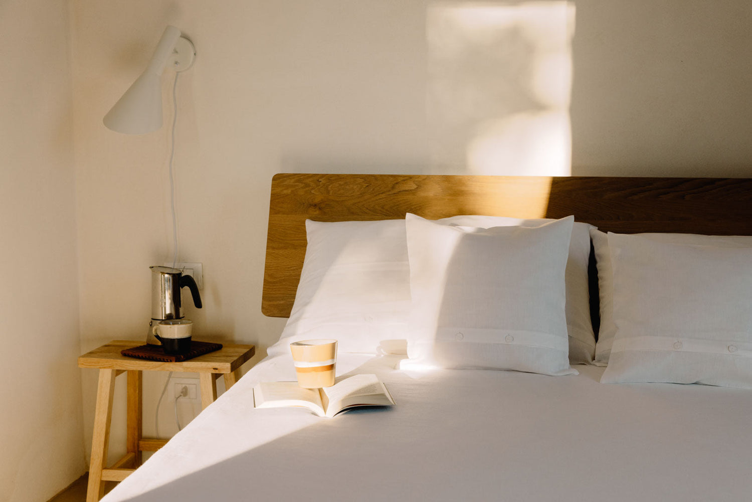 Bett mit Kopfteil aus Holz und weißer Leinenbettwäsche und Nachttisch aus Holz daneben