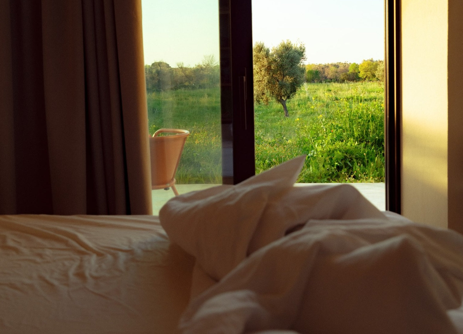Im Bett mit heller Bettwäsche mit Blick aus dem geöffneten Fenster ins Grüne
