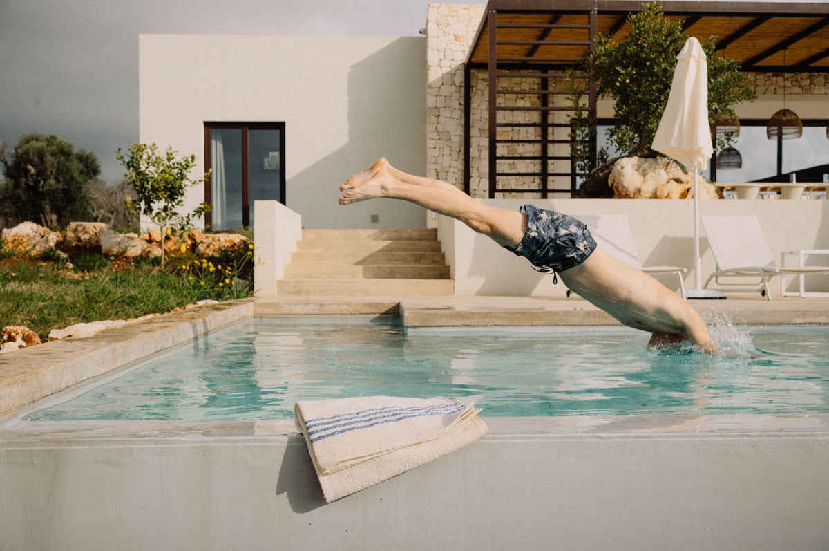 Mann springt mit Kopfsprung in Pool, am Poolrand liegt Handtuch aus Leinen.