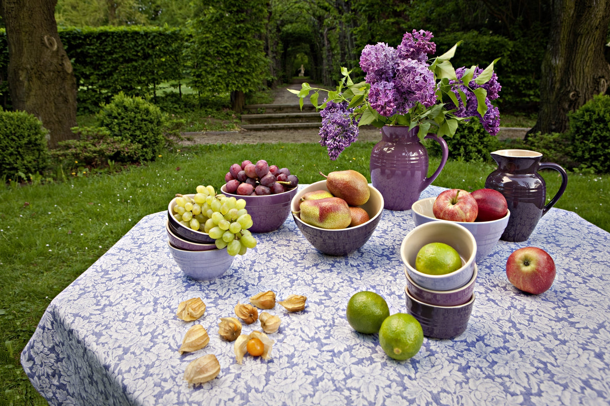 Gedeckter Tisch im Garten mit einer Leinentischdecke mit Röschen-Muster.