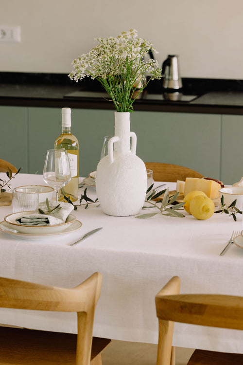 Gedeckter Tisch mit weißer Leinentischdecke, Gläsern und Olivenzweigen