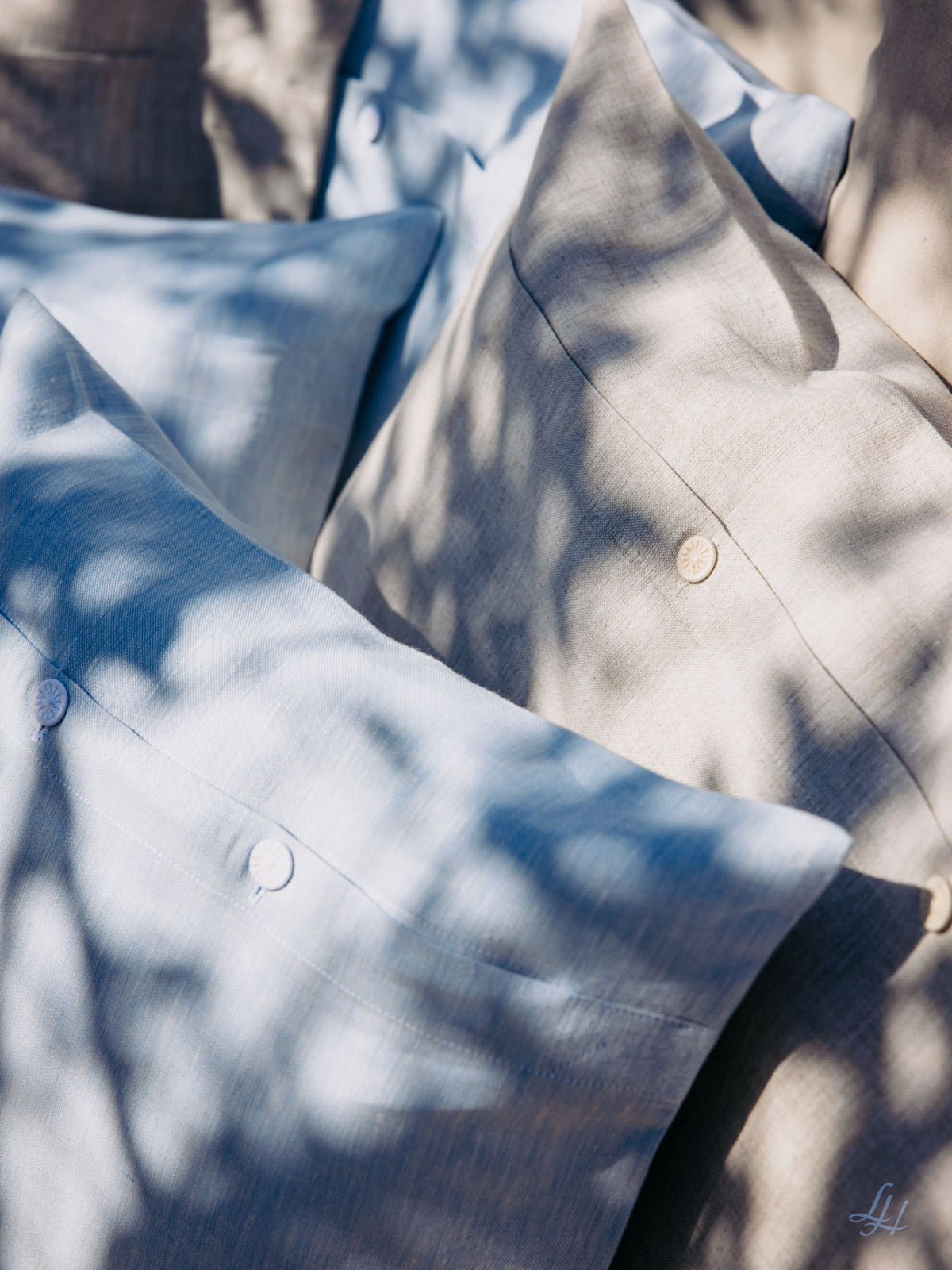 Nahaufnahme eines hypoallergenen Leinen-Kissenbezugs in Hellblau und Beige, der von Sonnenlicht und Schatten der nahen Äste durchdrungen ist.