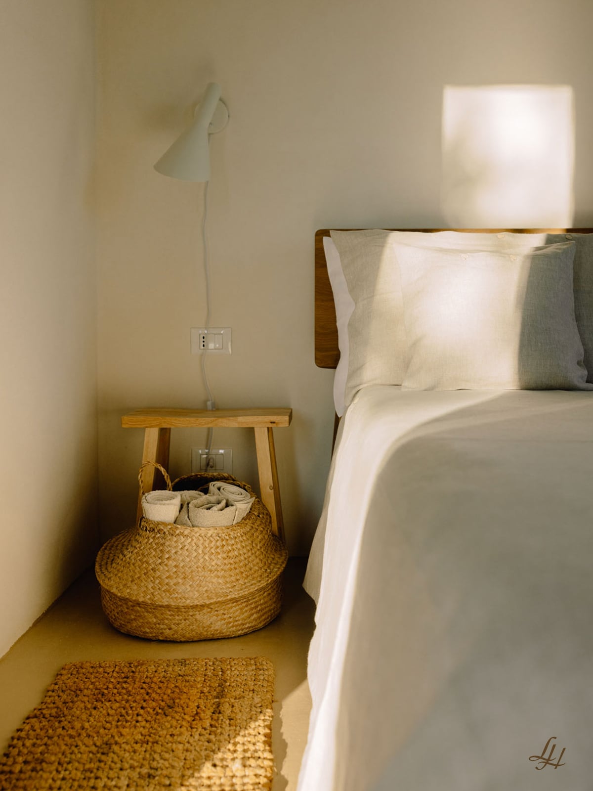 Ein Nachttisch mit Weidenkorb, Naturtöne-Handtuch und Lampe neben einem Bett mit einem atmungsaktiven Leinen-Kissenbezug.