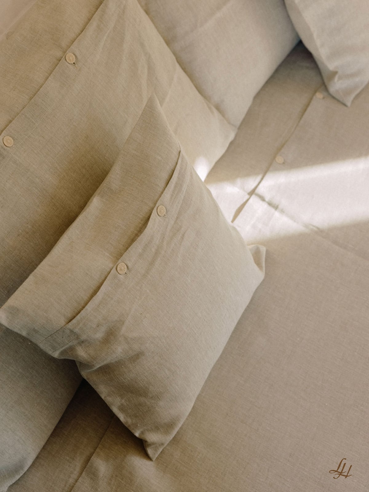 Beige Leinen Kissenbezug mit Button-Details auf Sofa oder Bett, Naturtöne und atmungsaktiv im Sonnenlicht.